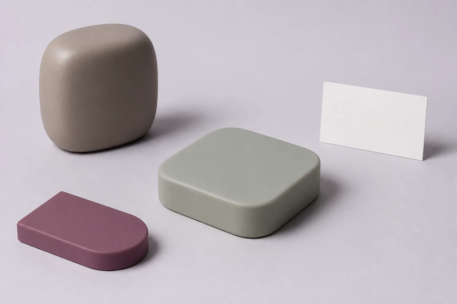 Illustrative UHMW request-planning arrangement with one unmarked muted mineral ochre-grey opaque compact upright box-superellipsoid with one gently flattened edgeless upper surface, one integral flat underside and one continuous broadly curved closed exterior and one separate unmarked dusty-plum opaque low flat-sided half-oval-footprint solid beside one monolithic pale sage-grey opaque low rounded-square-footprint solid with one broad unmarked flat rounded-quadrilateral top face, one continuous plain outward-convex side surface, a fully closed envelope and no opening, and one completely blank upright matte-white landscape-proportion card