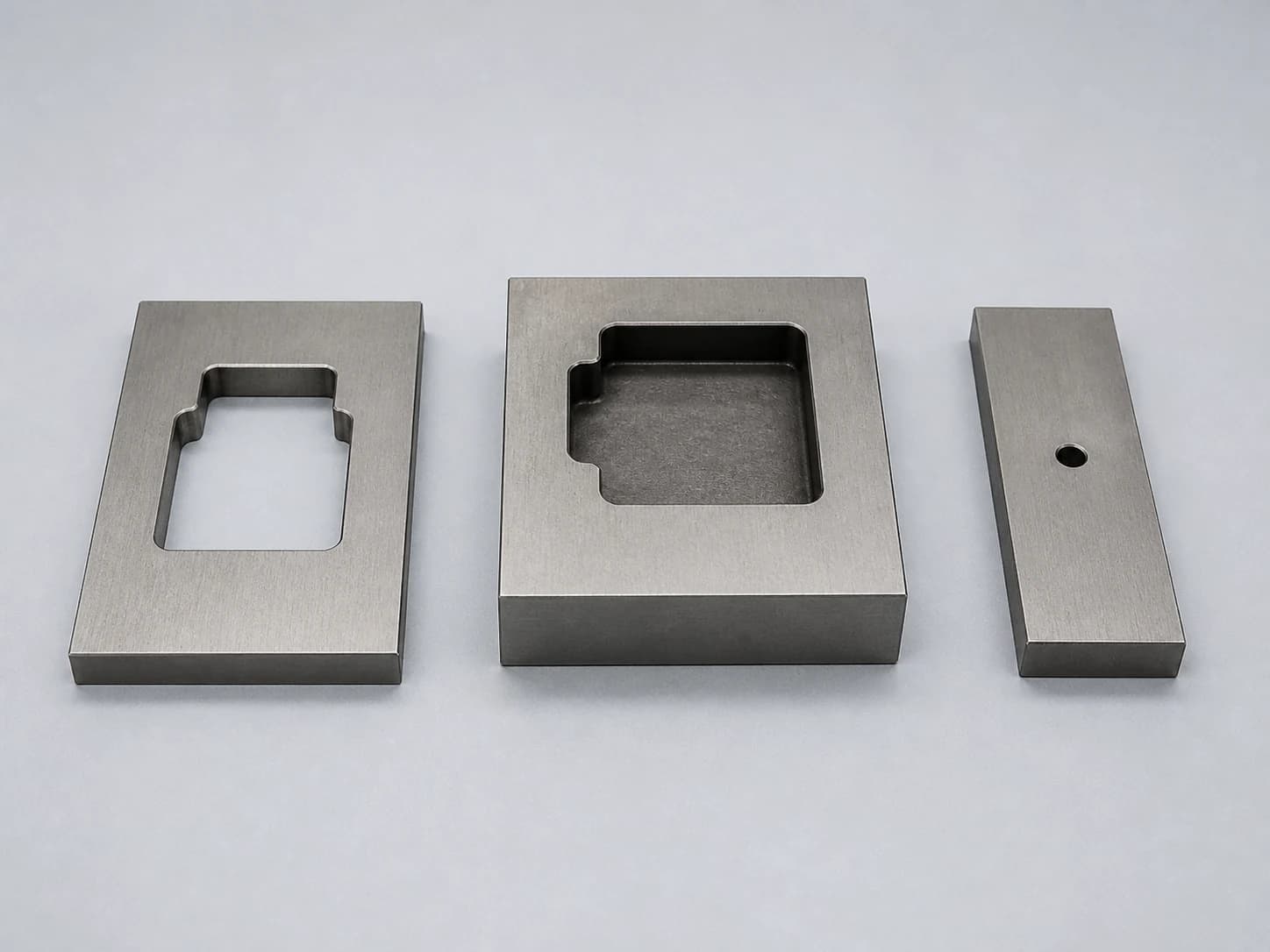 Illustrative hardened tool-steel EDM demonstration inserts showing a wire-cut profile, a blind sinker cavity, and a small EDM start hole
