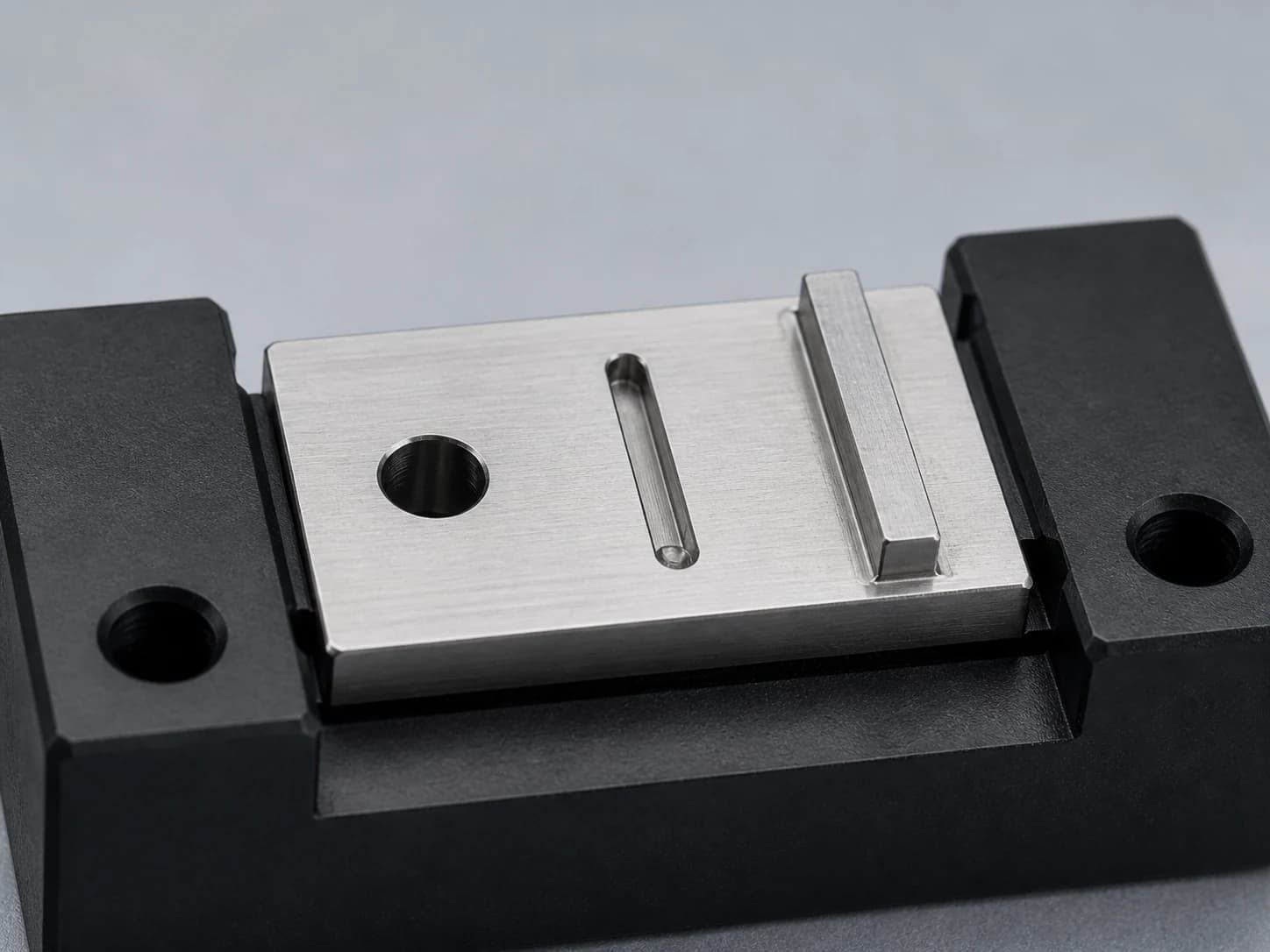 Illustrative miniature machined stainless steel component showing a small through-hole, a fine slot, and a thin supported wall